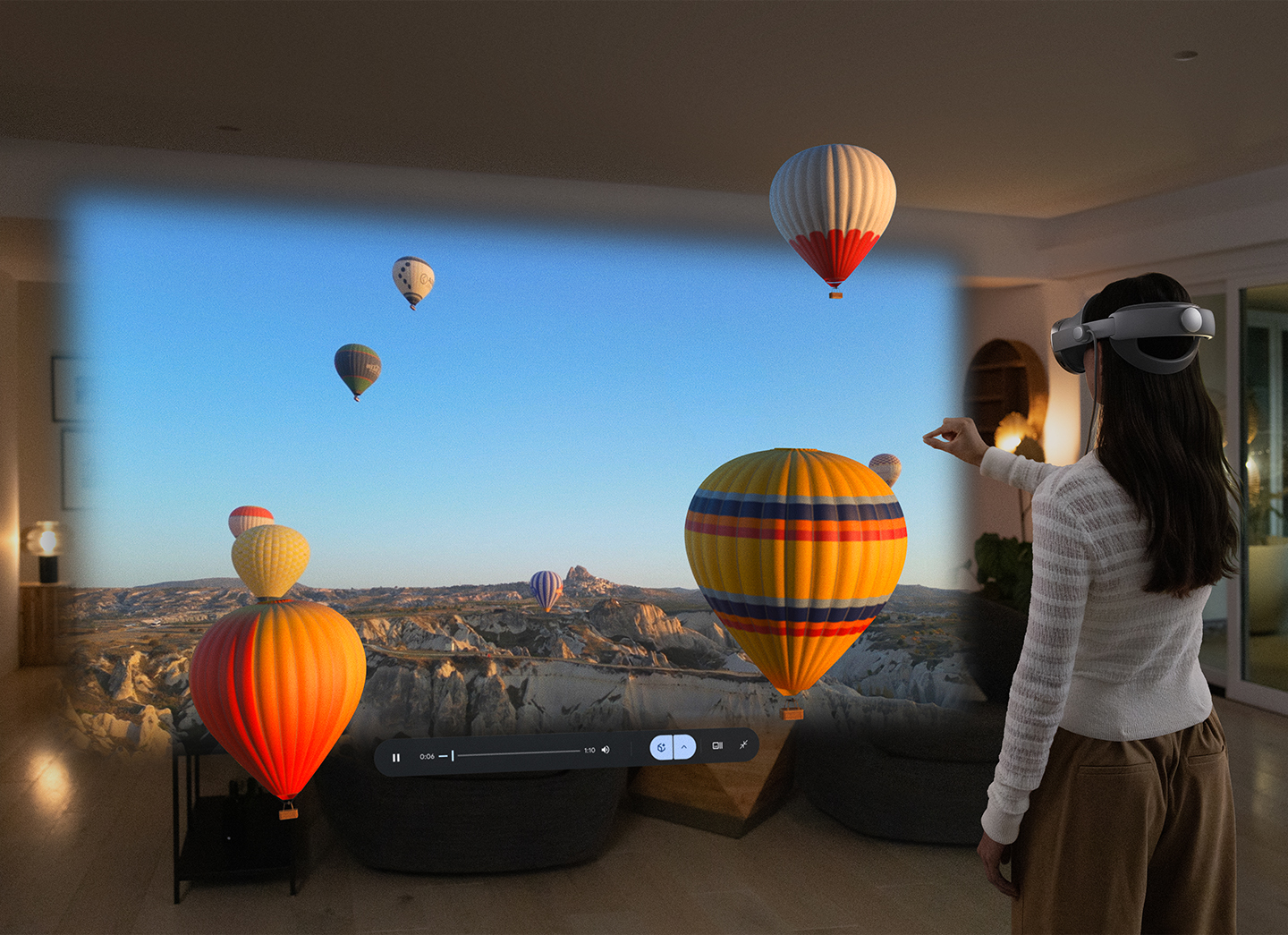 A woman wearing a Galaxy XR headset stands in her living room as a virtual background of Cappadocia hot air balloons appears to emerge from the screen in front of her.