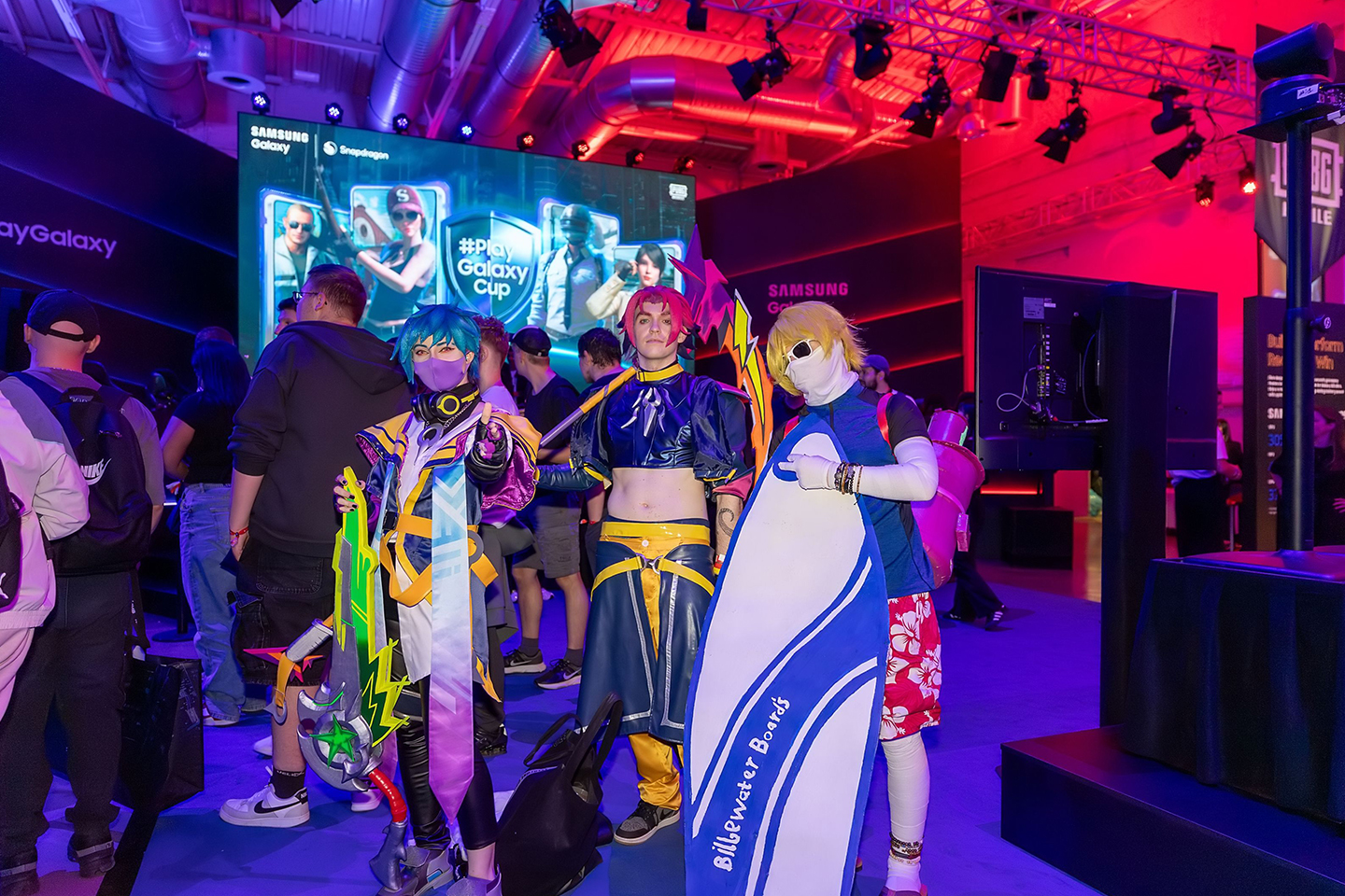 Three people in cosplay costumes are posing for the camera at The World of PlayGalaxy gameplay booth.